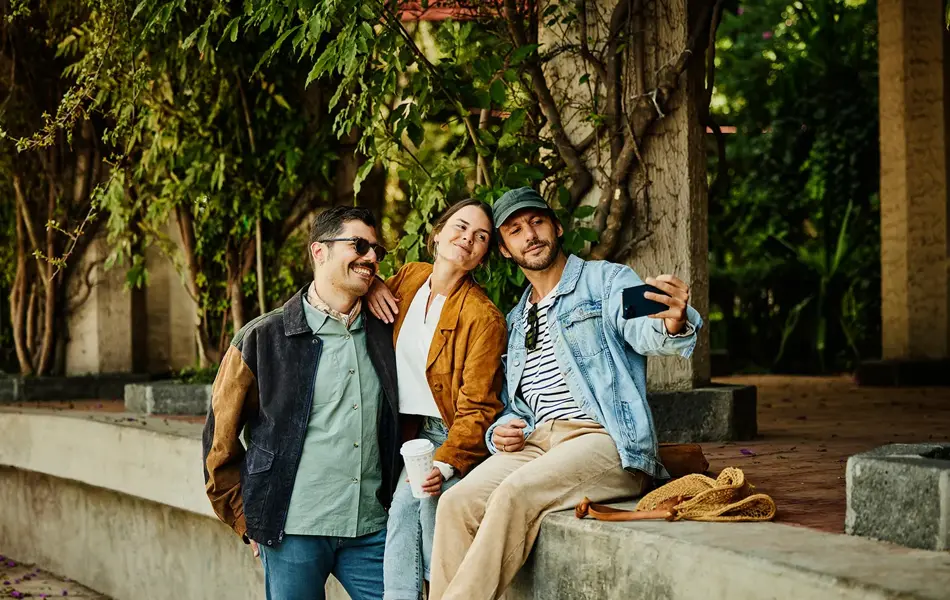 Tre venner tar selfie sittende på en murvegg 