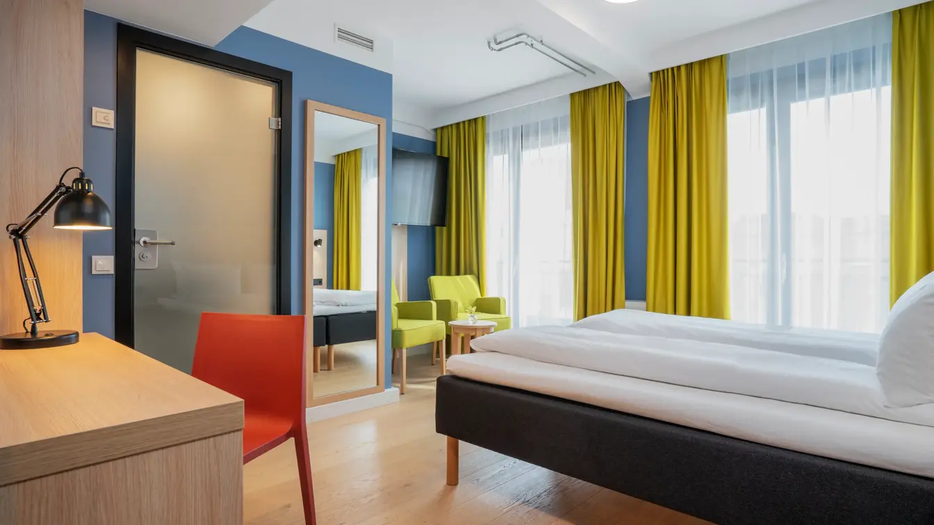 Skrivebord med rød stol, speil, blå vegger, dobbeltseng og gule gardiner i dobbeltrom på Thon Hotel Astoria