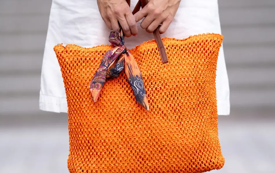 Dame i hvit kjoled holder en orange flettet veske med skinnhanker.