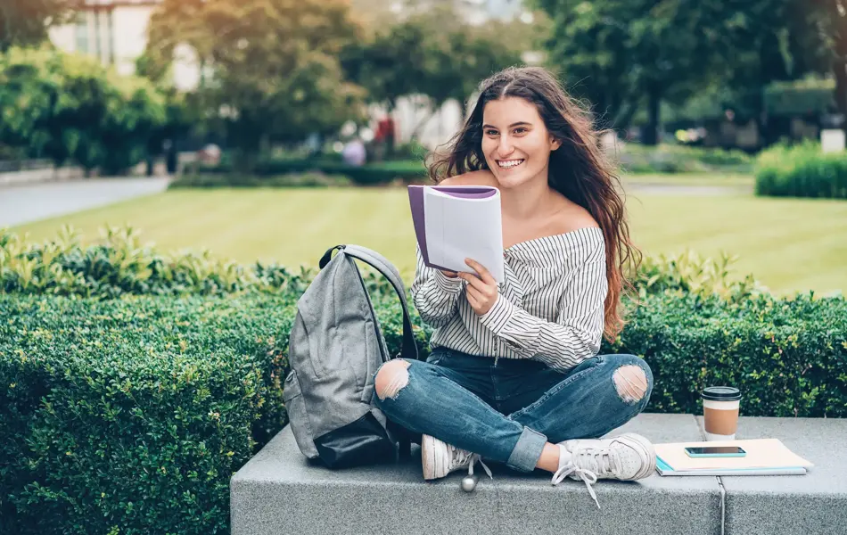 Student sitting outdoors and writing in a notebook