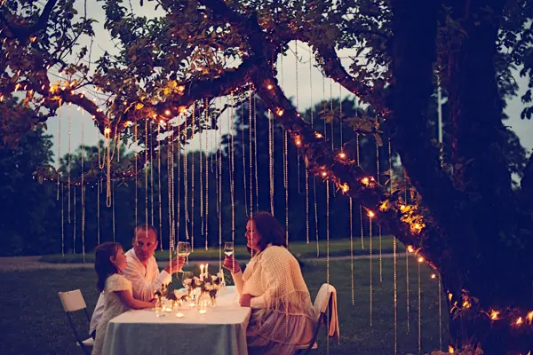 Gruppe ved bordet om kvelden med dekorasjoner hengende fra trærne over