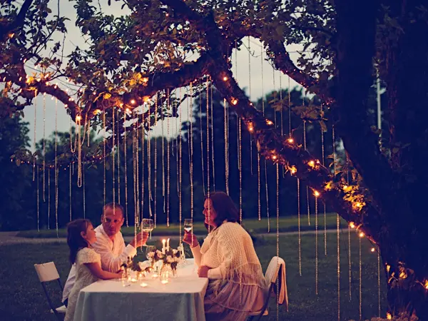 Gruppe ved bordet om kvelden med dekorasjoner hengende fra trærne over