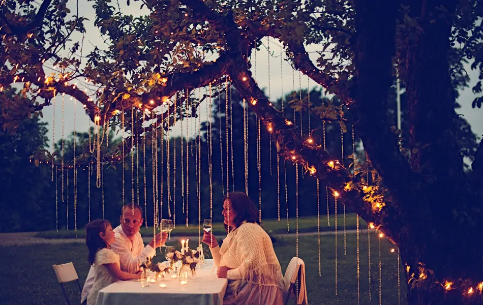Gruppe ved bordet om kvelden med dekorasjoner hengende fra trærne over