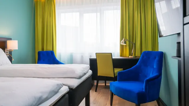 Twin room med hvit sengetøy, gule gardiner, skrivepult og blå lenestol på Thon Hotel Europa i Oslo sentrum rett ved Slottsparken