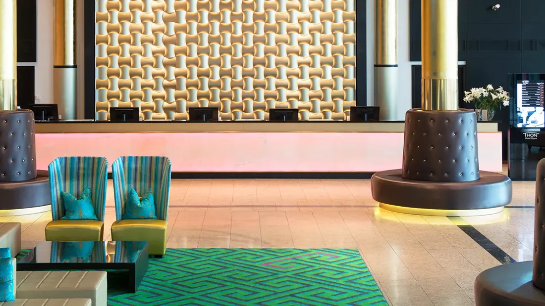 Resepsjonsområdet hos Thon Hotel Opera, med sittegrupper, sitteplasser rundt søyler, gullbelagt bakvegg i resepsjonen.