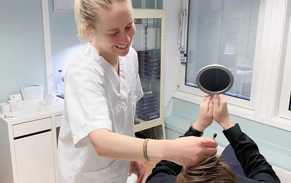 Dame ser seg i håndholdt speil mens smilende pleier holder instrument i pannen 