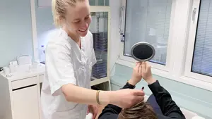 Dame ser seg i håndholdt speil mens smilende pleier holder instrument i pannen 