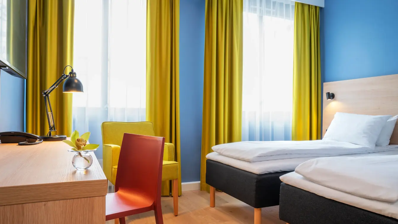 Separate senger, blå vegger, gule gardiner og skrivebord på standard rom twin på Thon Hotel Astoria