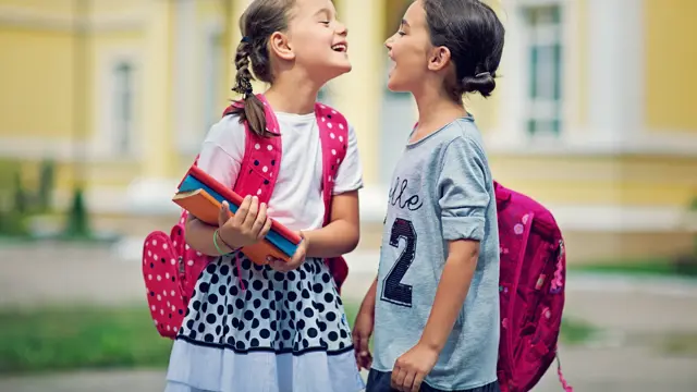 Two schoolgirls are making fun in the school yard at first day at school

