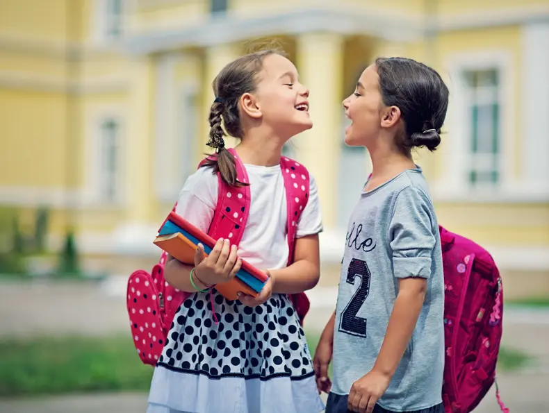 Two schoolgirls are making fun in the school yard at first day at school


