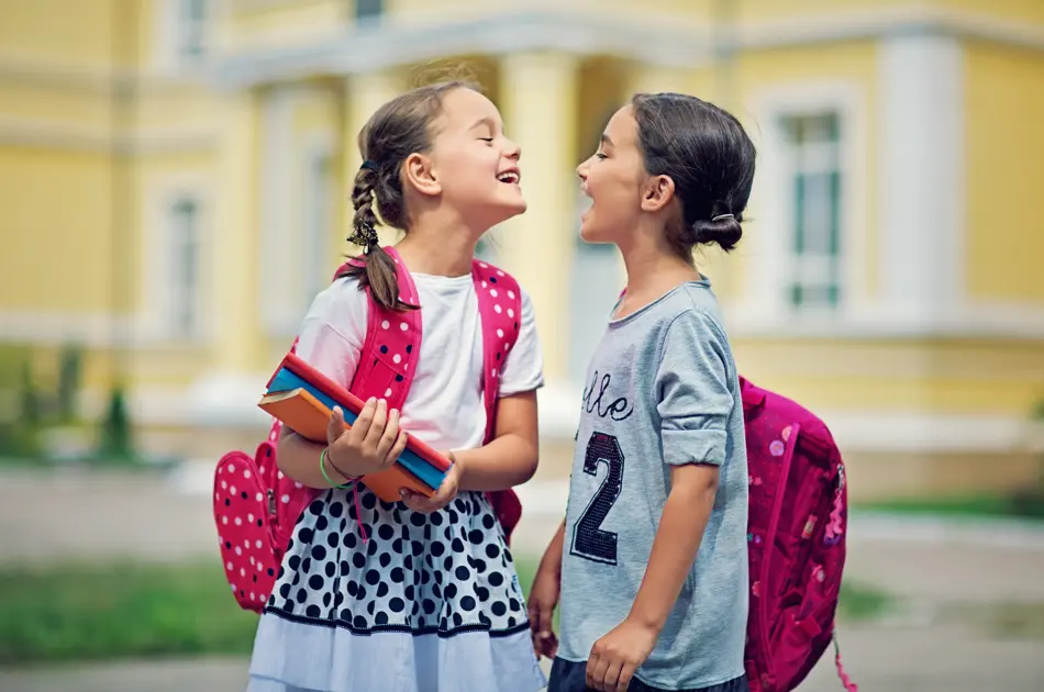 Two schoolgirls are making fun in the school yard at first day at school

