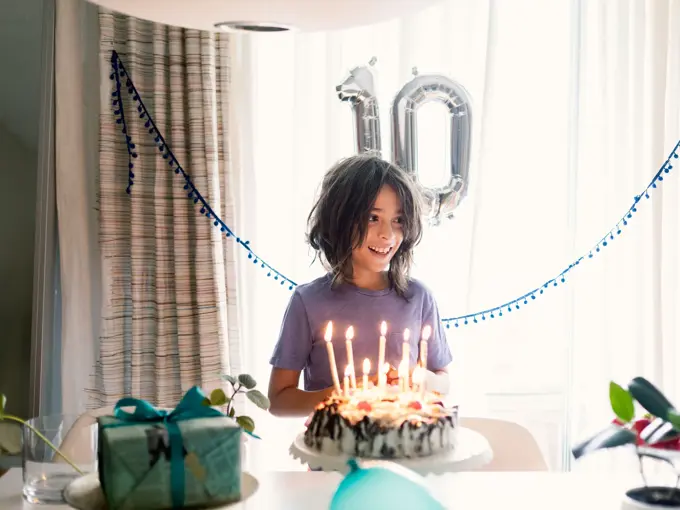 Gutt står i rom med kake, gaver og ballonger som viser tallet 10
