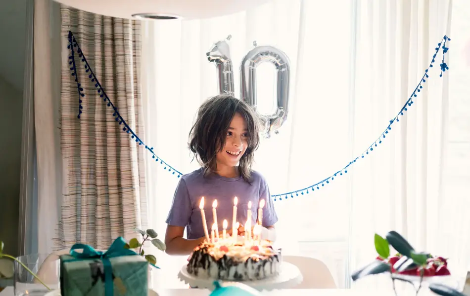 Gutt står i rom med kake, gaver og ballonger som viser tallet 10