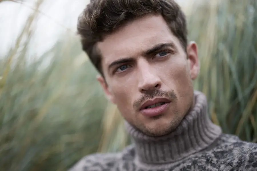 Mann i høyhalset strikkegenser sitter i gresset og ser bort