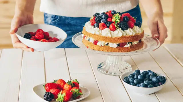 Nærbilde av hender som presenterer kake med krem og skogsbær. Foto til artikkel om dekorasjoner til 17. mai.