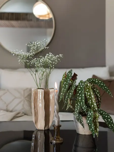 En vase med blomster og en grønn potteplante og et brennende lys på et stuebord