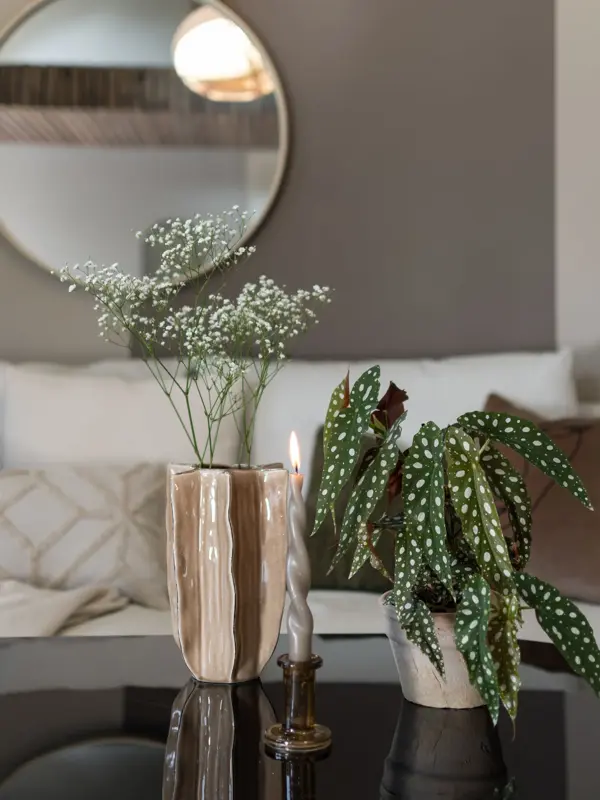 En vase med blomster og en grønn potteplante og et brennende lys på et stuebord