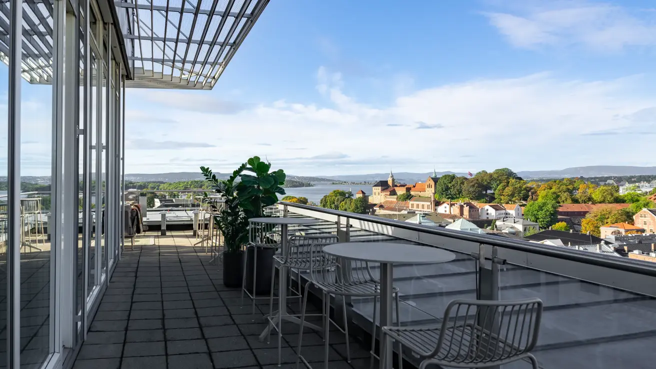 Terrasse med høye stoler og høye bord med utsikt over Oslo i fint vær