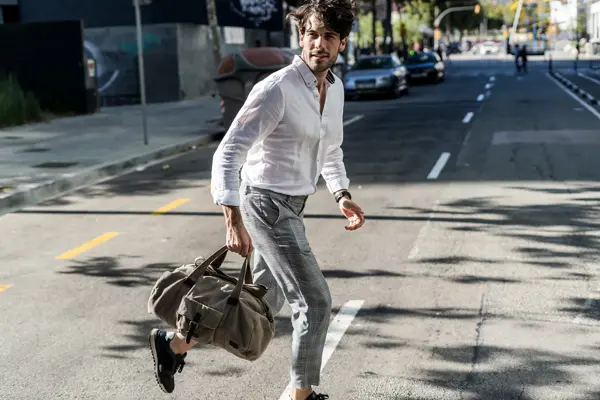 Mann med hvit skjorte, grå slimfit dressbukse og grå bag løper over veien 