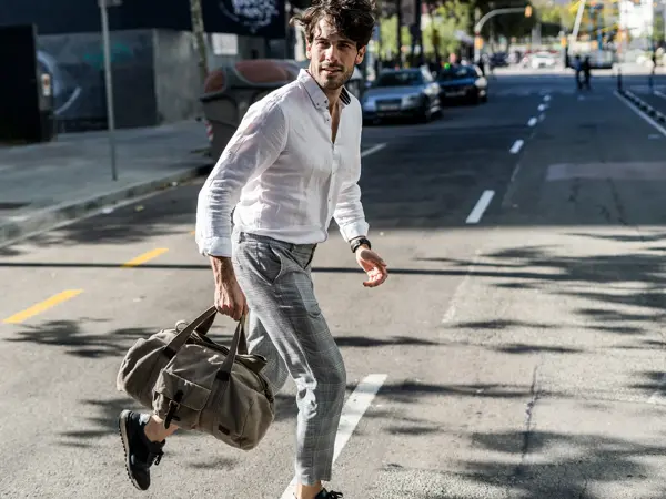 Mann med hvit skjorte, grå slimfit dressbukse og grå bag løper over veien 