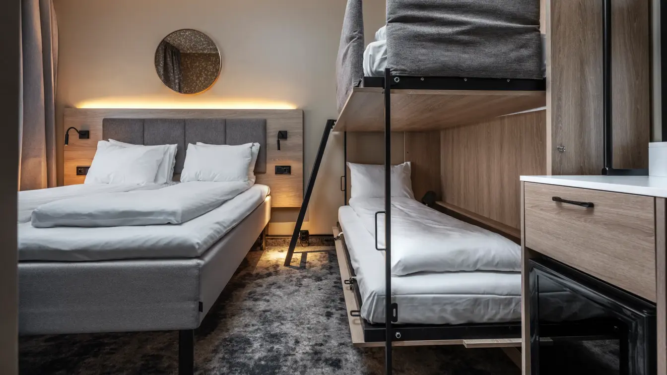 Dobbeltrom med queen seng og oppredd køyeseng ved siden av. Lys rundt sengegavl, minibar og gulvteppe.