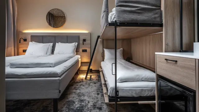 Dobbeltrom med queen seng og oppredd køyeseng ved siden av. Lys rundt sengegavl, minibar og gulvteppe.