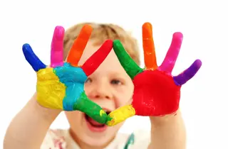 Five year old boy with hands painted in colorful paints ready for hand prints