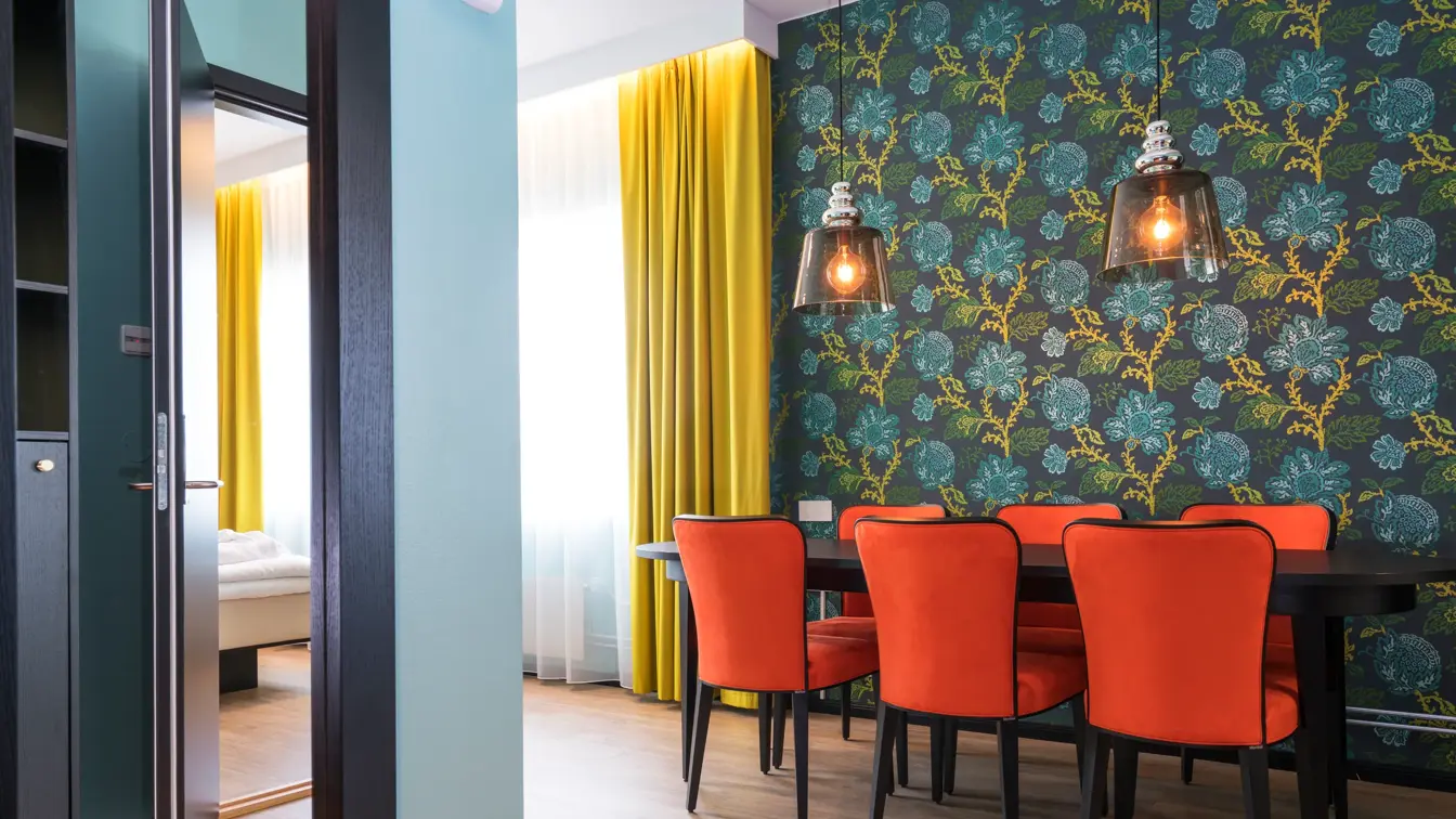 Suite fellesareal med spisebord, røde stoler og gule gardiner