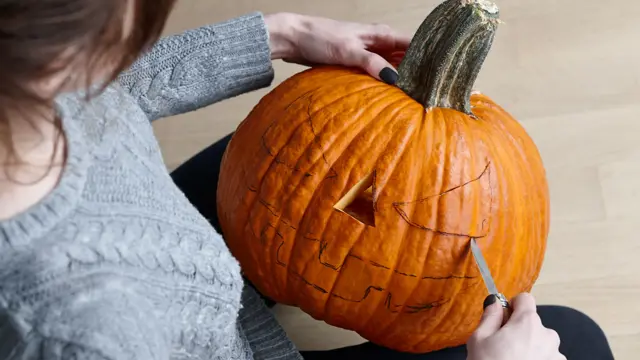 Woman carving big orange pumpkin into jack-o-lantern for Halloween holiday decoration, close up view
