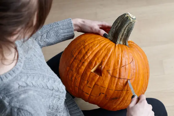 Woman carving big orange pumpkin into jack-o-lantern for Halloween holiday decoration, close up view