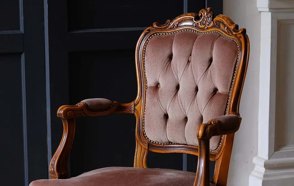 Antikk stol i barokk stil med bølgende tre og mørke, gammelrosa puter. Interiørtrend vår 2022.