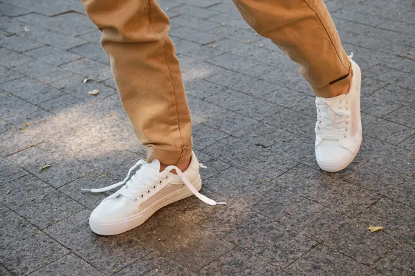 Manneben med brun bukse og hvite joggesko går på gata 