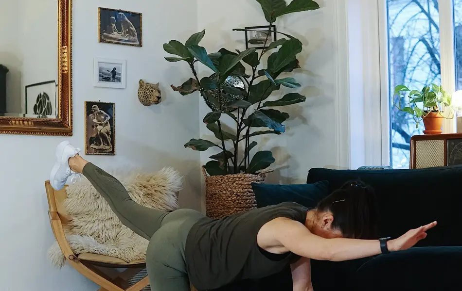 treningsekspert Anna Johansen trener på matte på gulvet, mørkegrønn sofa i bakgrunnen, lys stol med pels oppi, str grønn plante, bilder på veggen