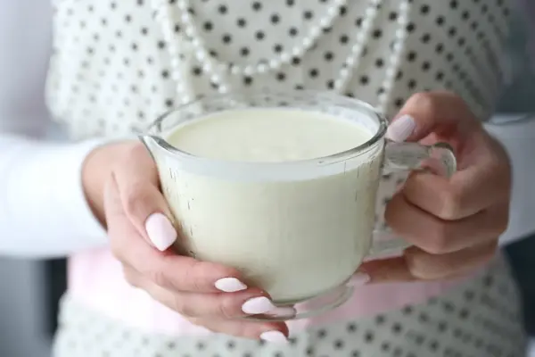 Hender som holder et målebeger med fløte