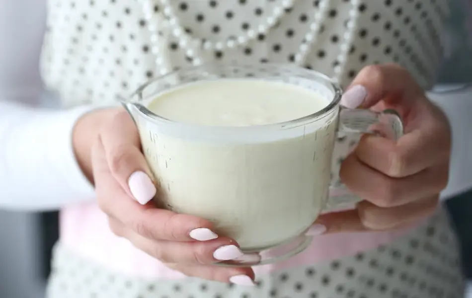 Hender som holder et målebeger med fløte
