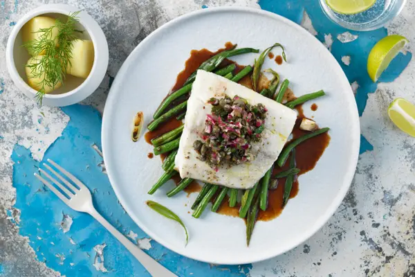 Borddekning med en tallerken med kveite på en seng av aspargesbønner 