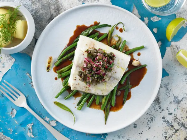 Borddekning med en tallerken med kveite på en seng av aspargesbønner 