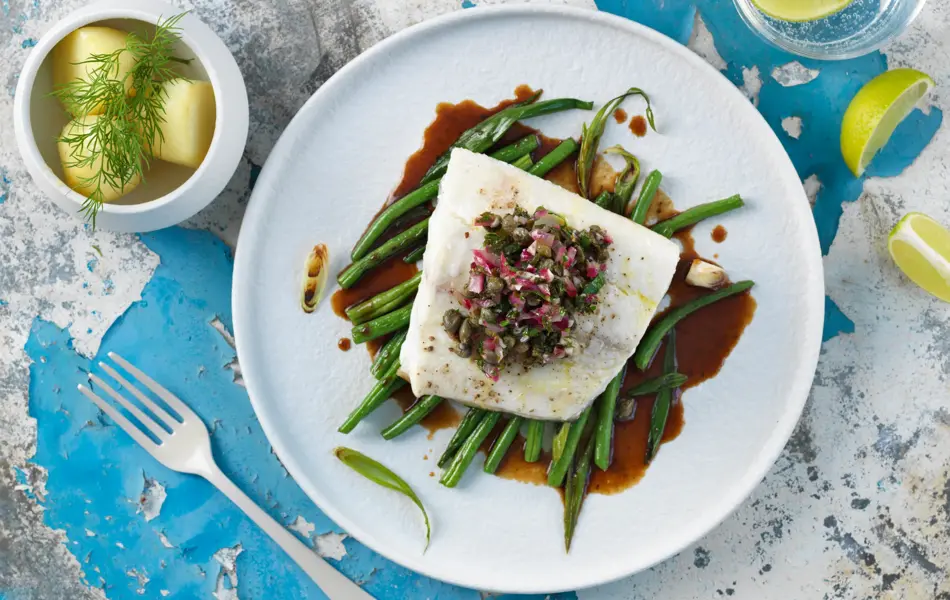 Borddekning med en tallerken med kveite på en seng av aspargesbønner 