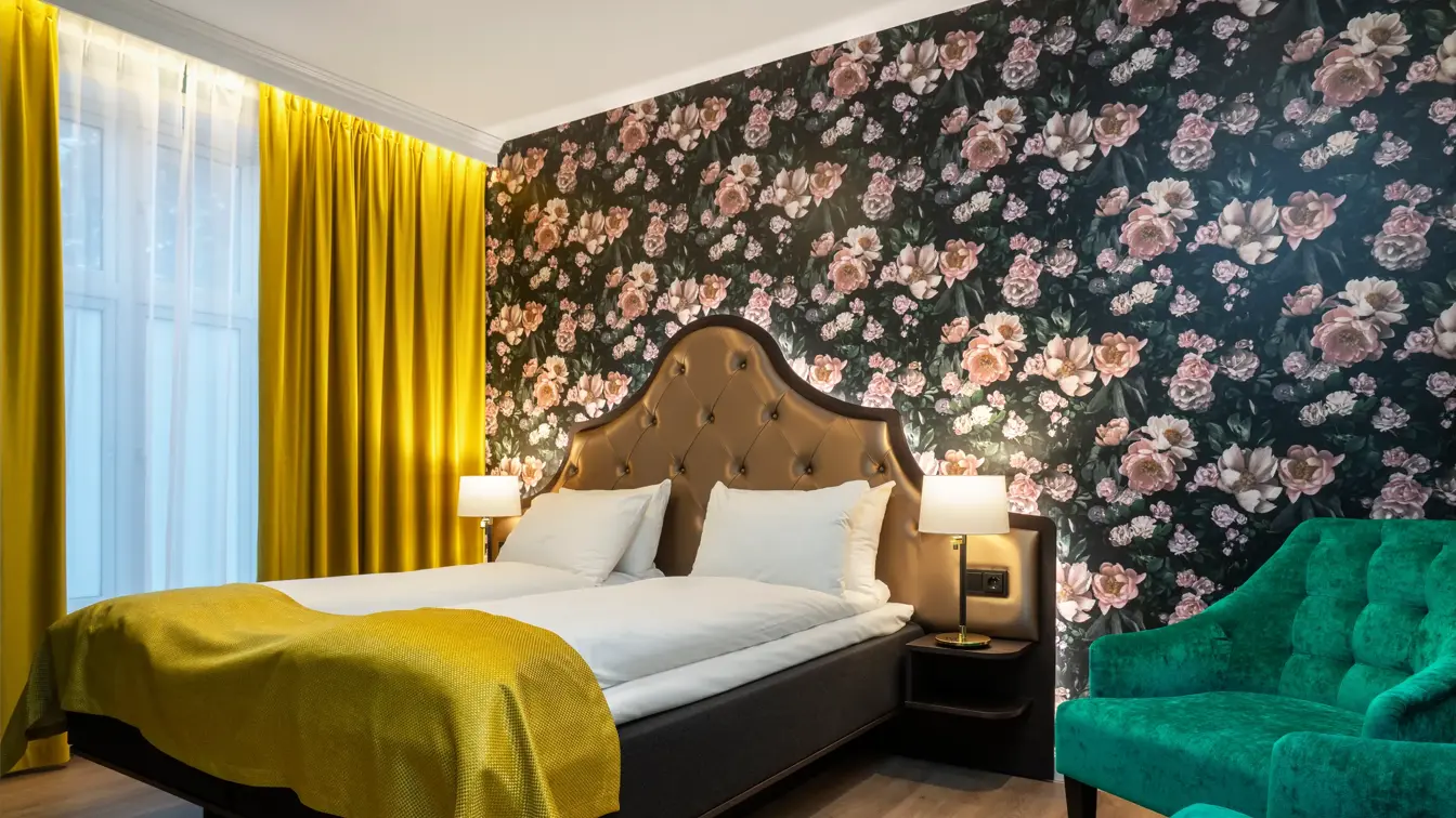 Mørk tapet med store lyserosa roser. Stort vindu med gule gardiner fra tak til gulv. Dobbeltseng med gult sengeteppe. To grønne lenestoler. I business rom på Thon Hotel Høyers i Skien.