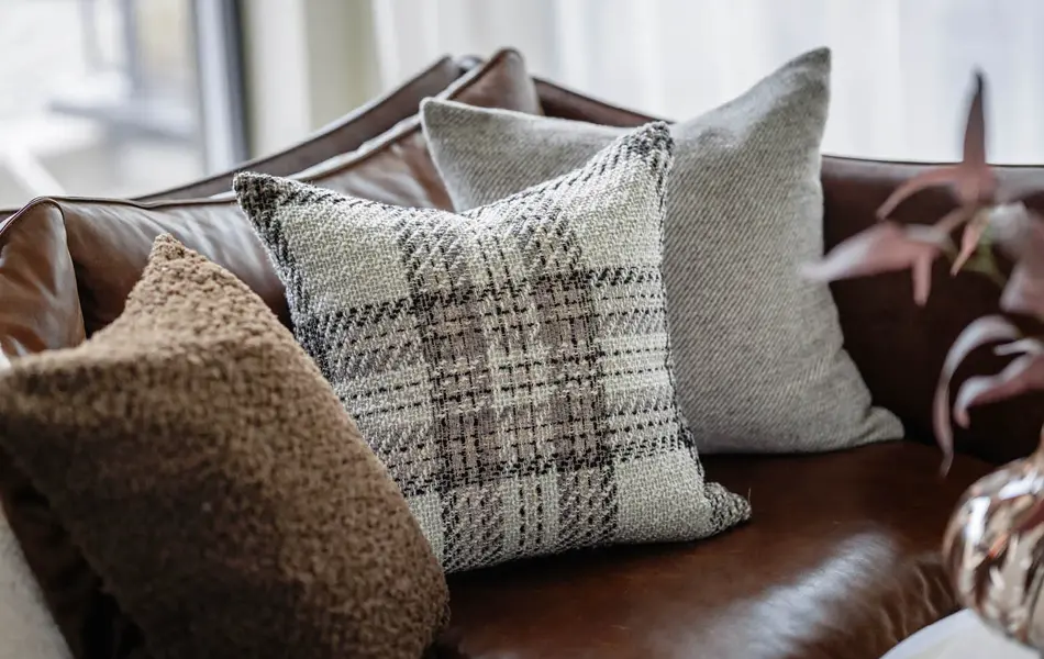 Hjørne av brun skinnsofa med tre puter.