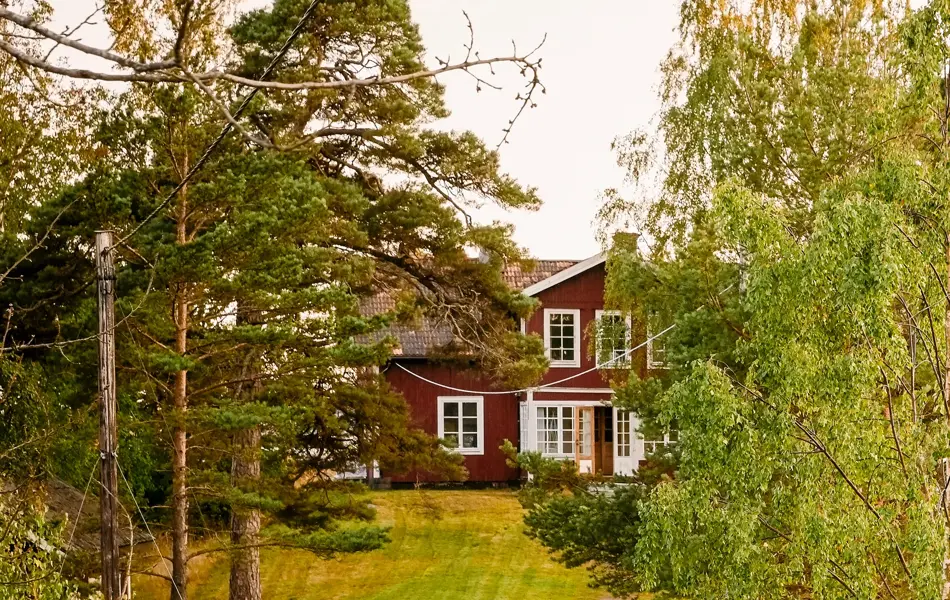 Rødt hus hytte ved kysten, to mennesker går på grusvei.