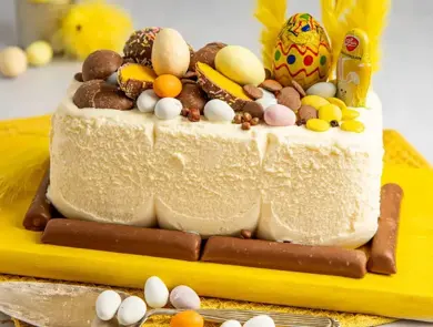 En kremfarget iskrem som er tatt ut av isboksen og dekorert med masse påskegodt og gule fjær