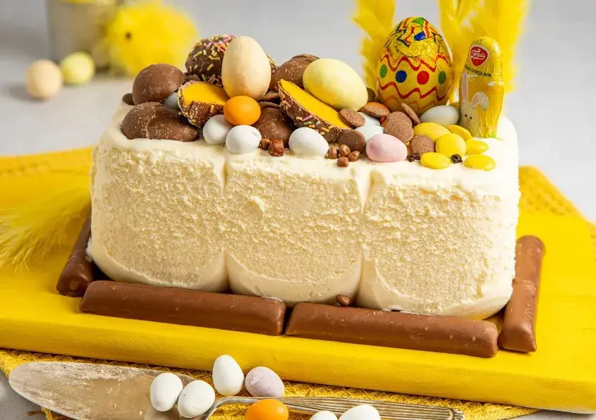 En kremfarget iskrem som er tatt ut av isboksen og dekorert med masse påskegodt og gule fjær