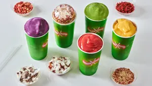 Fem smoothier i grønne beger med shavings ved siden av