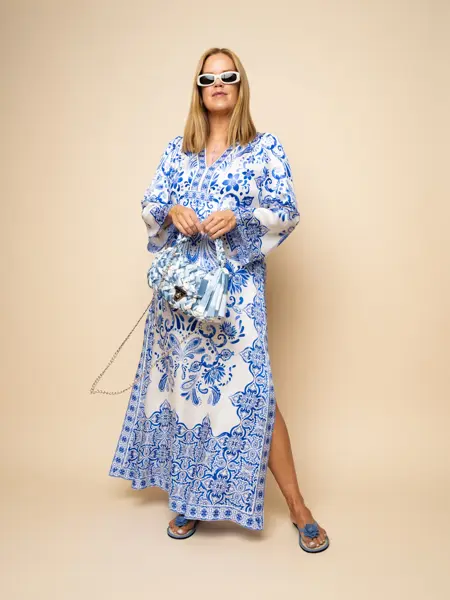 Damemodelle i blåmønstret kjole og veske, blå flip flops og hvite solbriller