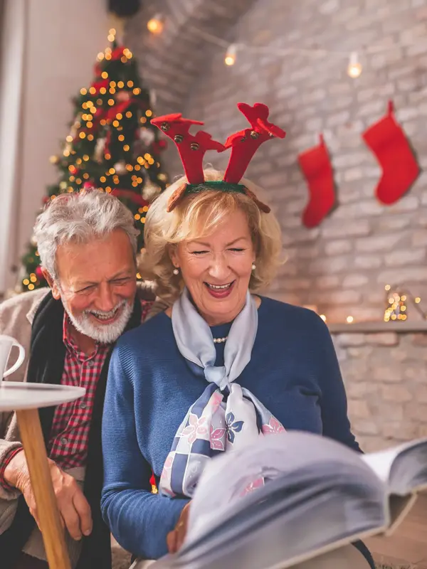 eldre mann og dame som ser på fotoalbum med juletre i bakgrunnen