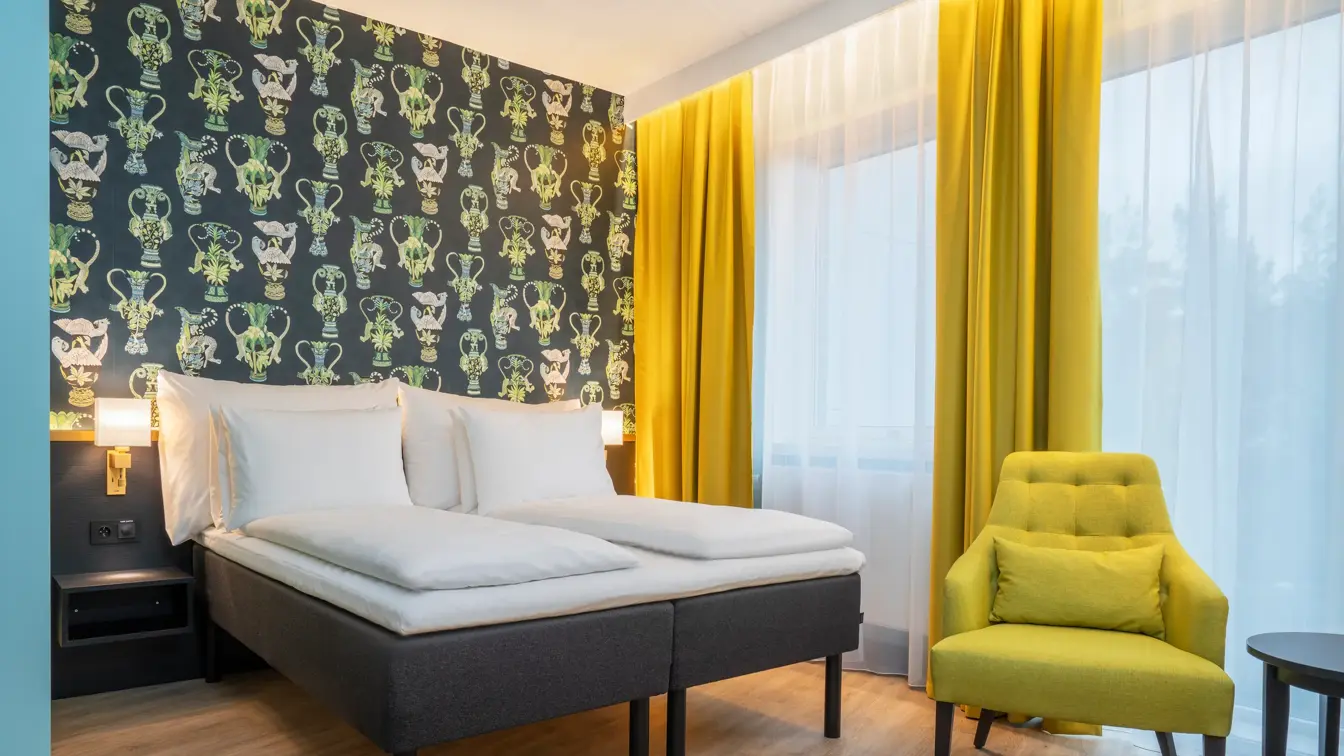 Mønstrete tapet med grønne detaljer, dobbeltseng, gule gardiner og gul stol i business rom på Thon Hotel Linne