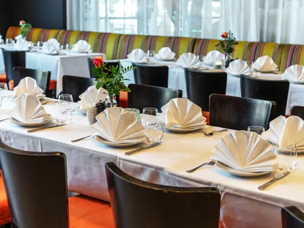 Oppdekket langbord med hvit duk, brettede servietter på tallerken og bestikk.