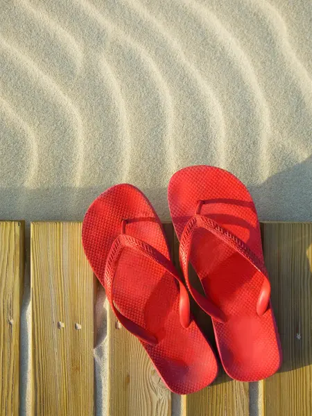 Et par røde flip flops ligger på treplanker på sandstrand 