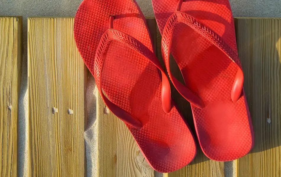 Et par røde flip flops ligger på treplanker på sandstrand 